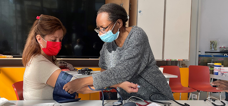 A community health worker with the InTOuCH program conducts a blood pressure check on another woman.