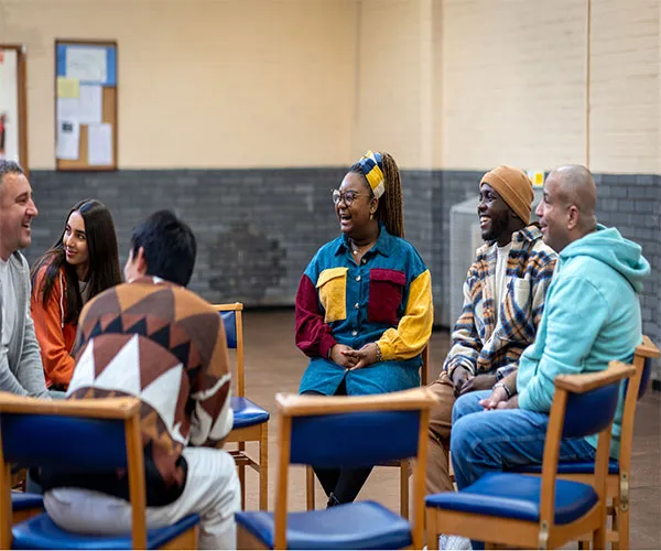 Group of men an women are seated in chairs in a circle conversing 