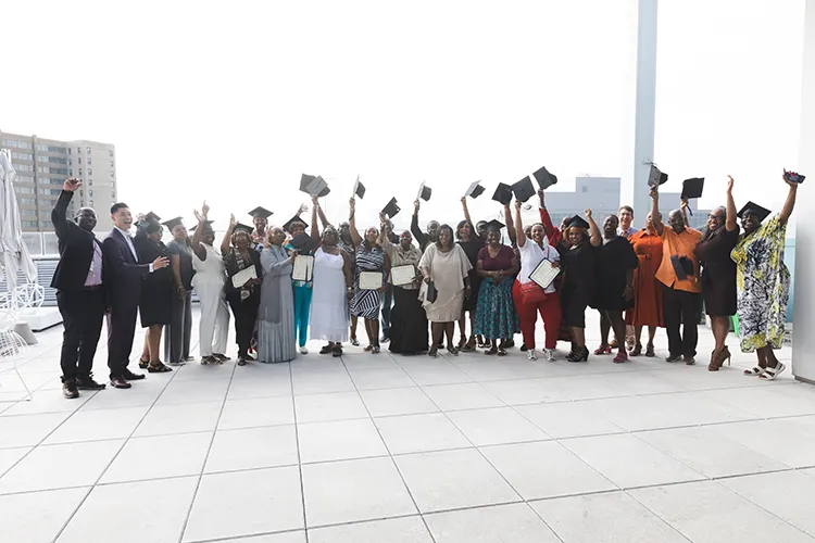 Exterior shot of multiple graduates of cohort 15 celebrate while holding caps and certificates 