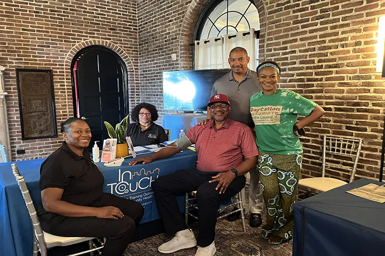 Various men and women stand and sit around an InTOuch draped table whle smiling into camera for a photo