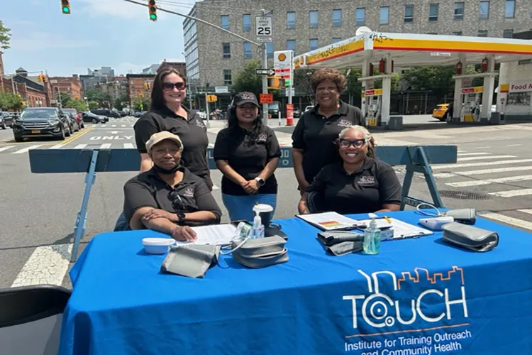 Exterior shot of InTOuch members seated and standing behind a table with supplies while smiling at the camera for the photo