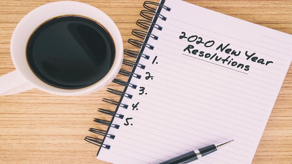 Cup of coffee and a pad with text 2020 New Year Resolutions with a pen sits on top of a wooden table