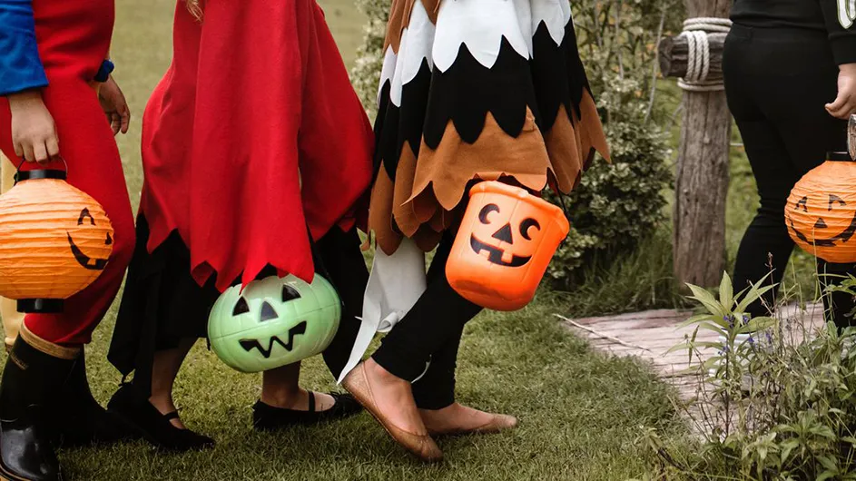 A group of kids wearing Halloween costumes and holding trick-or-treat buckets approach the door of a house.