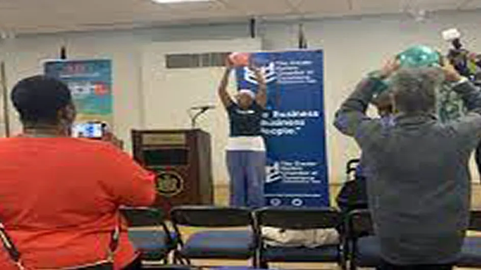 A group of people participate in an exercise by raising a ball above their heads.