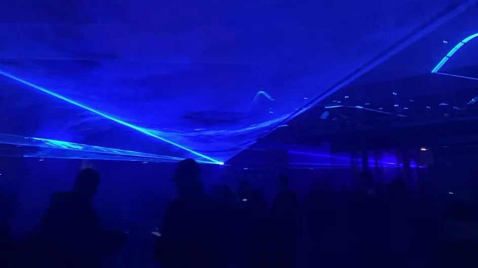 Rich blue laser lights surround a group of people observing an art installation. Photo Credit: Cindy Hsu