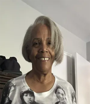 A woman wears a top depiicting historical female African American leaders whle smiling into camera. 