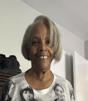 A woman wears a top depiicting historical female African American leaders whle smiling into camera.